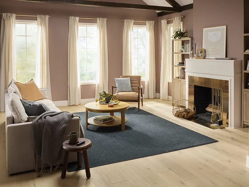 An elegant living room showcasing a large, gray and white distressed area rug over dark wood floors, with a button-tufted sofa and a fireplace.