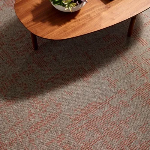 Close-up of textured gray commercial carpeting with red linear patterns beneath a wooden coffee table.