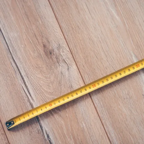 A yellow tape measure extended diagonally across light-colored wood flooring planks.
