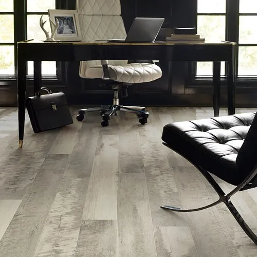 Grey, weathered wood-look laminate flooring in a contemporary home office with a sleek black desk and a white quilted office chair.